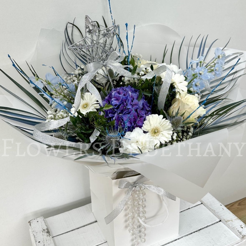 Stunning frozen themed bouquet filled with fresh florals. Design includes blue thistle, white germini, white rose, blue delphinium, blue hydrangea, white gypsophila, white carnations, palm leaves and finished with a removable silver star wand.